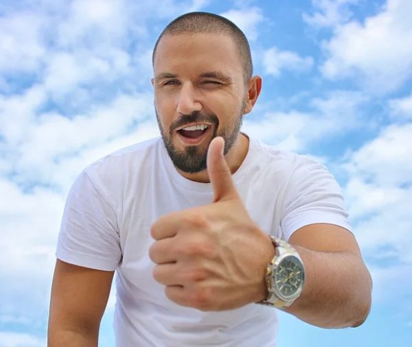 A man wearing a pilot watch, while doing the thumbs up sign.